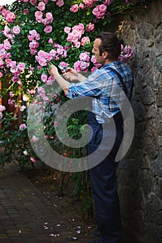 Full length portrait: male gardener floriculturist in blue gardening uniform, tending plants in the courtyard of mansion