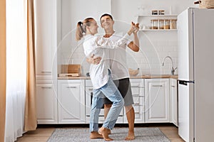 Full length portrait of man and attractive young adult woman dancing kitchen, romantic couple spending time together at home,