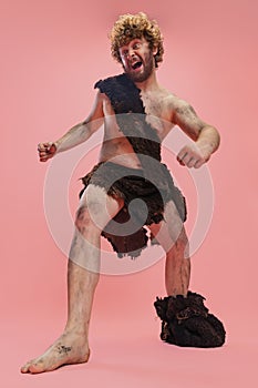 Full-length portrait of man in character of neanderthal wearing animal skin cloth and showing crazy movements isolated