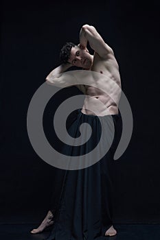 Full-length portrait of mature, muscular, handsome, shirtless man posing in dark fabric against black studio background