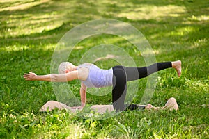 Full length portrait of a middle aged woman doing yoga or pilates on a mat outside in a park.Pose chakravakasana.