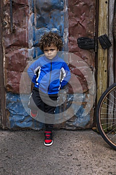 Full length portrait of an mixed race little boy standing on a dirty city street