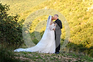 Full-length portrait of the newlyweds against the backdrop of brightly lit foliage, the newlyweds are kissing