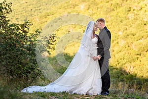 Full-length portrait of the newlyweds against the backdrop of brightly lit foliage, the newlyweds look lovingly at each