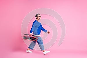 Full length portrait of nice aged lady walk hold boombox empty space wear blue sweater isolated on pink color background