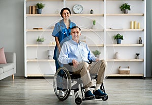 Full length portrait of older disabled man in wheelchair and his young caregiver smiling at camera in retirement home