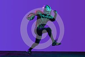 Full-length portrait of professional aerican football player in a run, training isolated over purple background