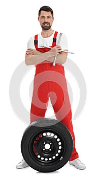 Full length portrait of professional auto mechanic with wheel and lug wrench on background