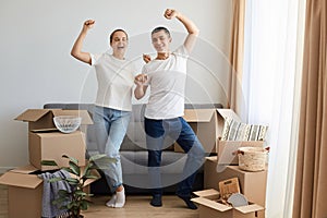 Full length portrait of satisfied woman and man wearing jeans and white t shirts posing among their belongings in boxes, standing