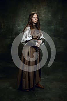 Full-length portrait of seriuos beautiful woman in image of medieval warrior or knight with dirty wounded face with big