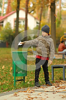 Full length portrait of a six year old boy throwing paper to the trash bin / garbage can in the park