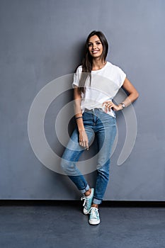 Full length portrait of a smiling casual woman standing on gray background. Looking at camera.