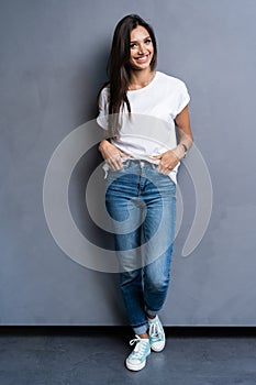 Full length portrait of a smiling casual woman standing on gray background. Looking at camera.