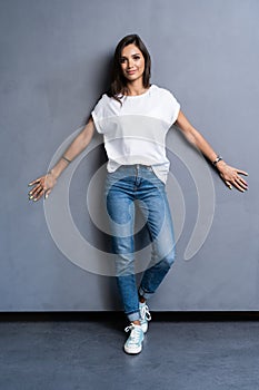 Full length portrait of a smiling casual woman standing on gray background. Looking at camera.