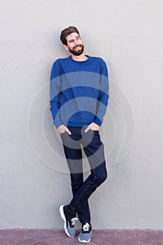 Full length smiling confident man leaning on white wall
