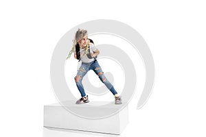Full-length portrait of smiling girl in casual clothes standing on big box isolated on white studio background. Happy