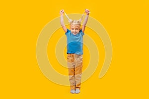 Full-length portrait of smiling little girl with two ponytails. Happy preschooler in blue T-shirt on yellow background