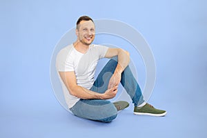 Full length portrait of a smiling man sitting on the floor against blue background