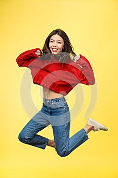 Full length portrait of a smiling pretty woman jumping  on a yellow background.