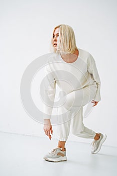 Full length portrait of smiling young blonde woman in sportswear on background of white wall