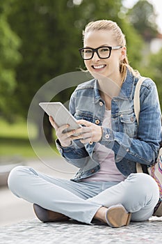 Full length portrait of smiling young female college student using tablet PC in park