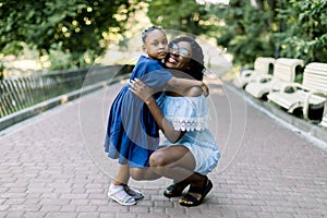 Full length portrait of smiling young happy african mother hugging her little baby daughter with tenderness and love