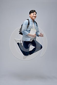 Full length portrait of a smiling young man dressed carrying backpack isolated, holding books, jumping