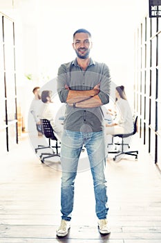 Full length portrait of smiling young man standing in doorway of office. Creative male executive at startup with people