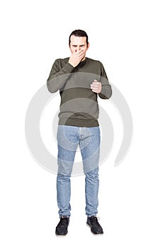 Full length portrait of a sneezing young man, covering mouth with his hand. Casual sick guy eyes closed, coughing in palm to stop