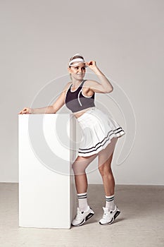 Full length portrait of sporty young adult woman with beautiful athletic body in fashionable sportwear standing and lean on