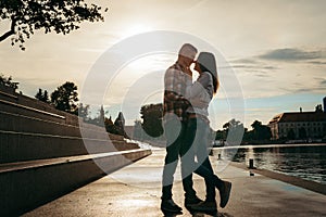 Full-length portrait in the street. Cheerful young pretty couple is hugging during the sunset. The girl is stroking the