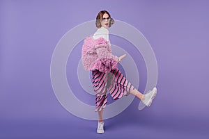 Full-length portrait of stunning female model wears trendy white sneakers and fur jacket. Studio ph