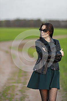 Full length portrait of a stylish girl walking along a green field. A young smiling woman is walking in nature. Green