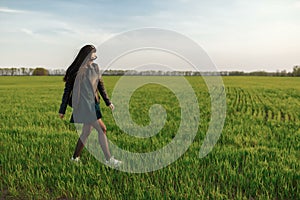 Full length portrait of a stylish girl walking along a green field. A young smiling woman is walking in nature. Green