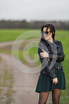 Full length portrait of a stylish girl walking along a green field. A young smiling woman is walking in nature. Green