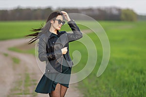 Full length portrait of a stylish girl walking along a green field. A young smiling woman is walking in nature. Green spring