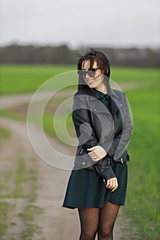 Full length portrait of a stylish girl walking along a green field. A young smiling woman is walking in nature. Green spring