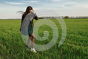 Full length portrait of a stylish girl walking along a green field. A young smiling woman is walking in nature. Green spring