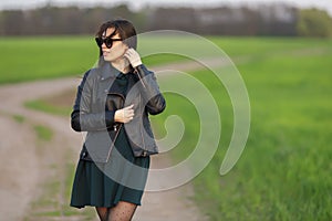 Full length portrait of a stylish girl walking along a green field. A young smiling woman is walking in nature. Green spring