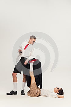 Full-length portrait of stylish young couple, man leaning on woman& x27;s legs, posing  over grey studio