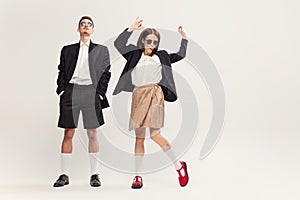 Full-length portrait of stylish young couple, man and woman in retro suit posing  over grey studio background