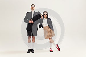 Full-length portrait of stylish young couple, man and woman in retro suit posing  over grey studio background