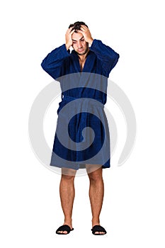 Full length portrait of tardy young man wears blue bathrobe holding hands to head, unable to wake up in time to get to work,