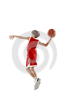 Full-length portrait of teen boy in red uniform training, playing basketball isolated over white background