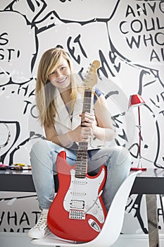 Full-length portrait of teenage girl with electric guitar sitting on study table at home