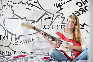 Full-length portrait of teenage girl playing guitar in bedroom