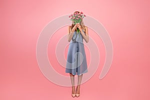Full length portrait of unrecognizable young lady covering face with bouquet of flowers on pink background, copy space