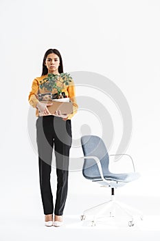 Full length portrait of upset young woman dressed in elegant wear holding box with office supplies due to firing