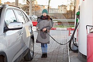 Full length portrait of woman holding fuel nozzle to add gas at petrol station, winter season