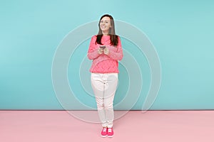 Full length portrait of woman in knitted rose sweater, white pants texting sms on cellphone isolated on bright pink blue